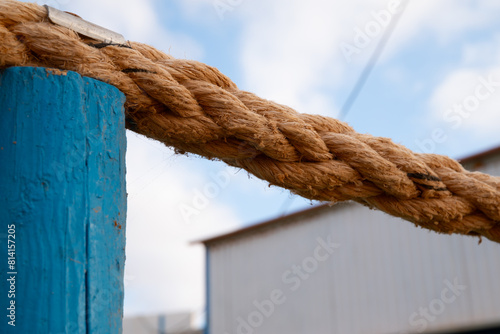A rope is tied to a blue pole. The rope is brown and has a lot of knots. The rope is tied to the pole in a way that it is not visible