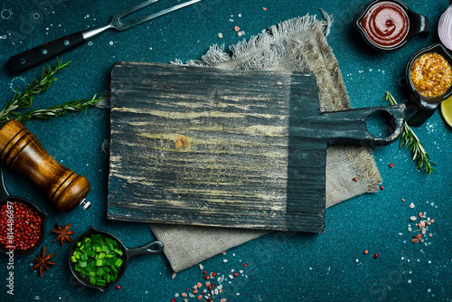 Kitchen cutting board on table with spices, vegetables and herbs. Free space for a recipe. Rustic style. On a dark background.
