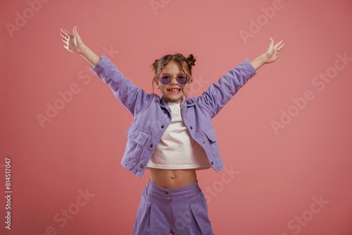Smiling, with hands up and on the sides. Cute little girl is against pink background