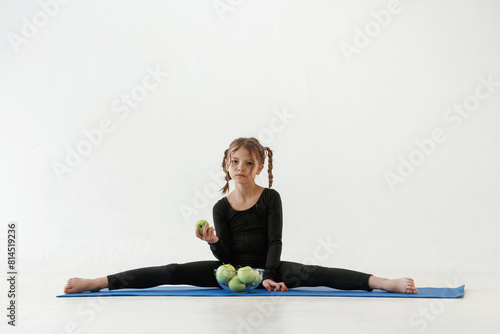 Healthy eating, green apples. Little girl in yoga clothes is on the fitness mat