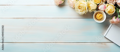 Top view of a modern feminine desktop workspace with a pink blue and yellow theme The stylish pale wood background is adorned with yellow roses creating a creative composition for a blog hero header