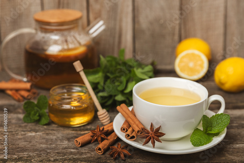 Fragrant hot tea with cinnamon stick and anise on a textured wooden background. A cup of hot tea with honey, lemon, mint and apples. Spicy tea with spices. Immunity tea. Health concept.Copy space.