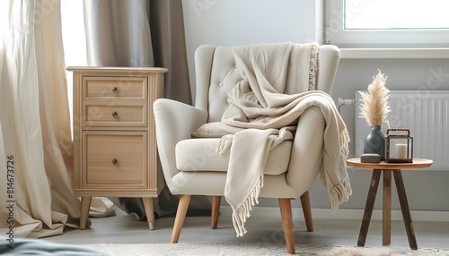 Comfortable armchair with blanket, side table and chest of drawers in room