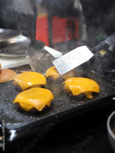 chef manipulando hamburguesas de carne con queso fundido con paletas de cocina en la parrilla