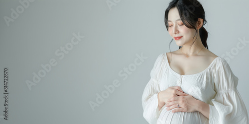 Pregnant Asian woman tenderly hugging her belly on a light gray background. The concept of preparing women for pregnancy, childbirth, motherhood. 