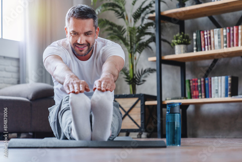Attractive sporty man stretching his legs at flat. Home training. Concept of sport, health, action, nutrition. Copy space for ad. Portrait of middle age sportive human guy doing stretching.