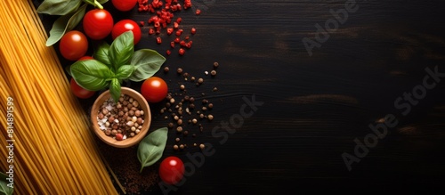 Top view copy space image of dark background with a variety of pasta ingredients including cherry tomatoes spaghetti pasta garlic basil parmesan and spices perfect for creating menus or trying out ne