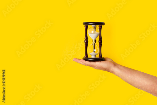 Mano de hombre sosteniendo un reloj de arena sobre un fondo amarillo brillante. Vista de frente y de cerca. Copy space