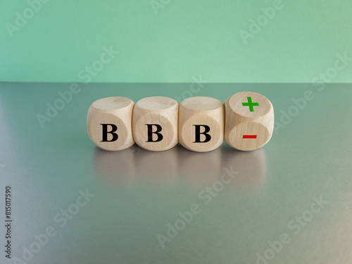 Symbol for a upgrade in a financial rating. Turned a wooden cube and changes the expression BBB minus to BBB plus. Beautiful blue background, grey table.