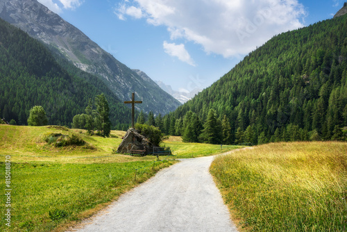 Mountain path and a christian cross in Prati di Sant'Orso. Cogne, Aosta Valley