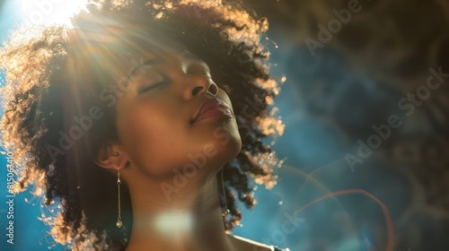 A woman's silhouette with curly hair backlit by a warm light creating a halo effect, emphasizing texture and shape