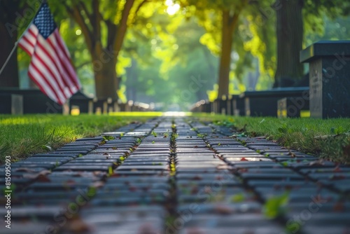  Low-angle view of a cobblestone path with an American flag, bordered by lush trees bathed in sunlight.