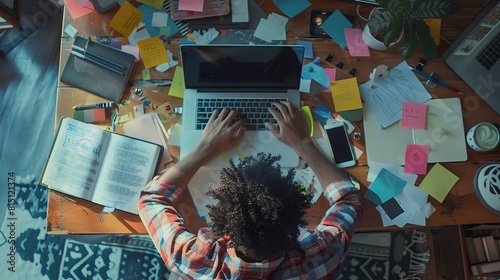 A person is working on a laptop in a messy home office.