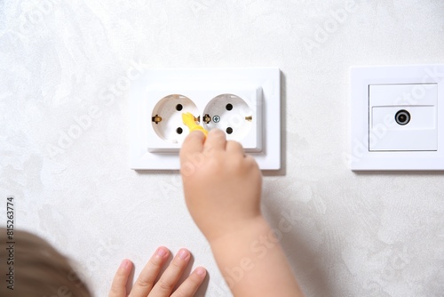 Little child playing with toy screwdriver and electrical socket at home, closeup. Dangerous situation