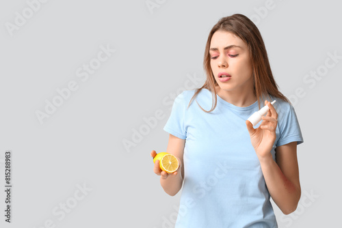 Young woman with lemon and nasal spray suffering from allergy on grey background