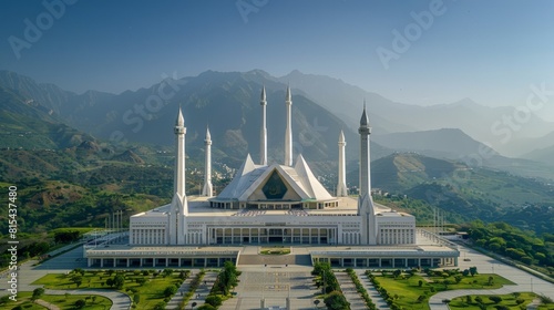 Aerial view of the Faisal Mosque in Islamabad, Pakistan, featuring its modern design with white minarets and tent-like structure set against the Margalla Hills. 