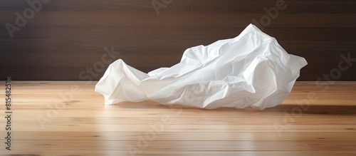 A crumpled white sheet of paper is seen in a lumpy state on a wooden floor creating a copy space image