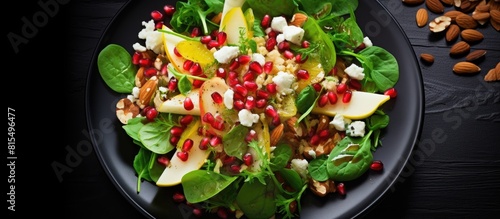 Healthy vegetarian food consisting of a salad composed of spinach leaves pear slices mixed nuts pomegranate seeds and feta cheese The dish is beautifully presented on a black plate and captured from