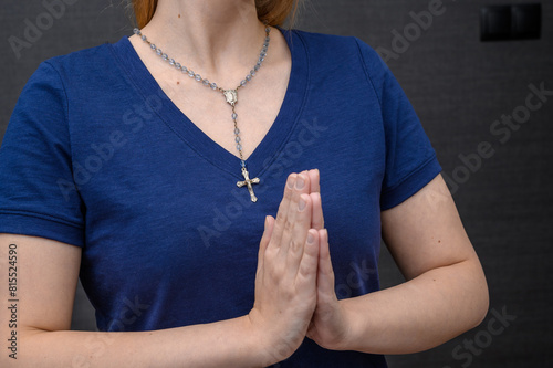 Młoda dziewczyna chrzecijanka katoliczka modli się, ma złożone ręce do modlitwy, na szyi różaniec z krzyżykiem 