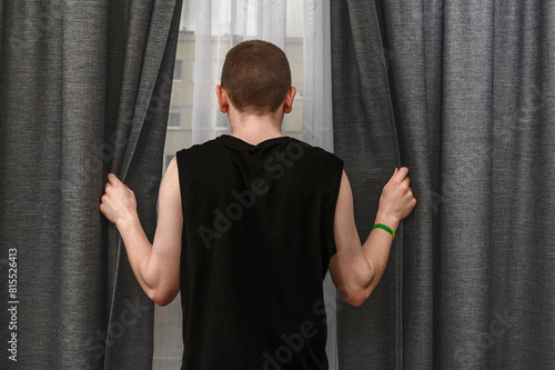 Samotny mężczyzna zasłania firanki w oknie, strach przed ludźmi, agorafobia 