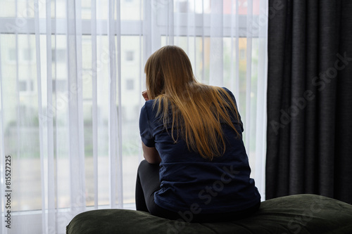 Kobieta w depresji siedzi w nowym mieszkaniu i patrzy przez okno