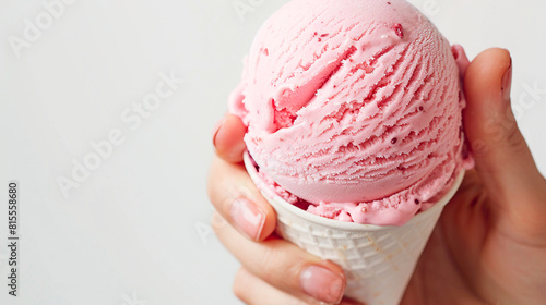 Cono de helado blanco con bola de color rosa de fresa sujetado por una mano en primer plano. Postre de helado para verano