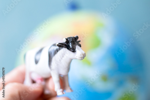 Plastic toy cow in front of world model background. Cows breeding and CO2 emission idea concept. Animal.