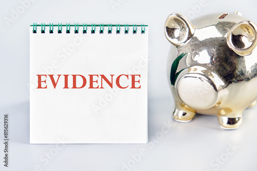 Business and finance concept. A word EVIDENCE on a vertically standing notebook near the piggy bank on a light background