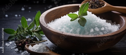 Big sea salt in a wooden bowl and spoon surrounded by herbs. copy space available