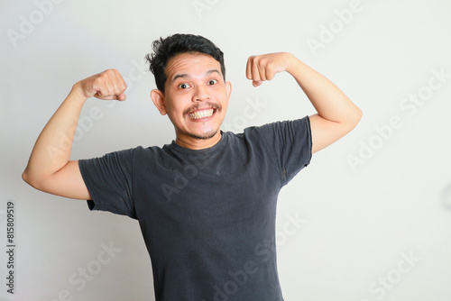 Adult Asian man showing excited expression by showing up his biceps muscle