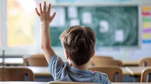 A smart schoolboy sits at a desk in a classroom with his hand raised, wanting to give the correct answer or participate. Concept of education, primary school, learning