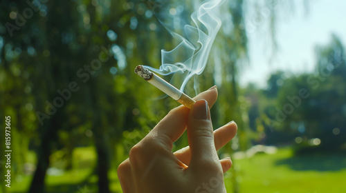 close-up of a hand holding a cigarette with smoke, background of green park, unhealthy lifestyle themeclose-up