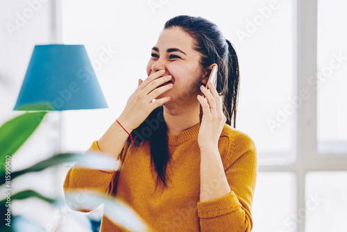 Emotional young woman laughing during mobile phone conversation with friend spending time at home interior,happy cheerful hipster girl satisfied with get exciting news while talking on telephone