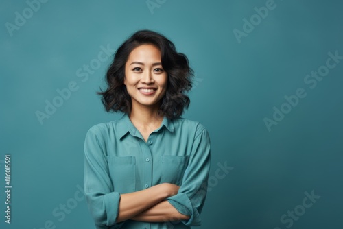 Portrait of a glad asian woman in her 30s with arms crossed over soft blue background