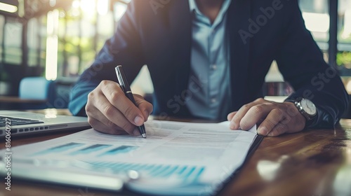 A professional businessman reviews complex financial charts and graphs while working at a wooden desk in a modern office setting..