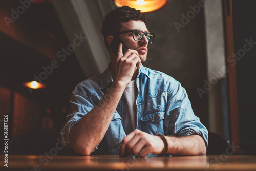 Young concentrated hipster guy thoughtful looking aside during important smartphone conversation, serious caucasian man calling to friend using mobile application and good wifi connection indoors