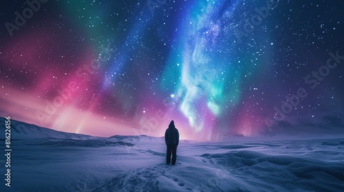 A person stands in snow field with beautiful aurora northern lights in night sky in winter.