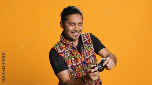 Happy gamer celebrating after winning game on gaming console, studio background. Delighted Indian man bragging after being victorious in videogame, defeating all enemies using gamepad, camera A