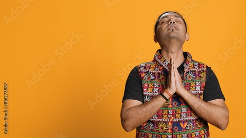 Pious indian man praying to his god, asking for forgiveness. Spiritual person doing worship hand gesturing, confessing, begging for pardon, isolated over studio background, camera A