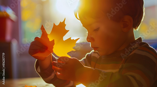 Boy in early development class cut paper and glue holding paper maple leaf : Generative AI