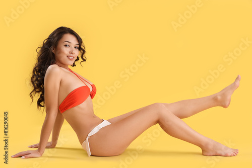 Beautiful young woman in swimsuit on yellow background