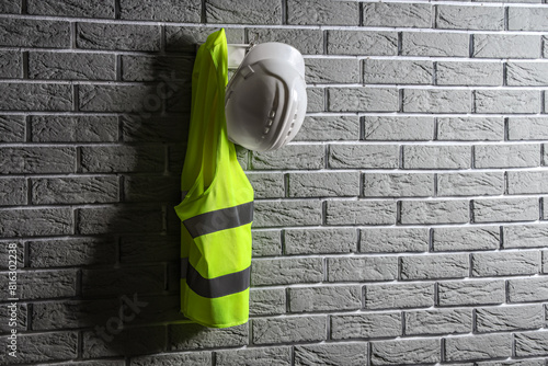 Safety vest and hardhat hanging on grey brick wall wall