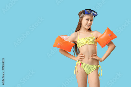 Cute little happy girl in swimsuit with inflatable armbands and snorkeling mask on blue background