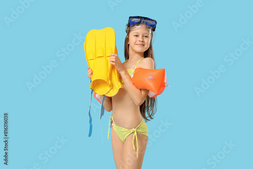 Cute little happy girl in swimsuit with inflatable armbands, flippers and snorkeling mask on blue background