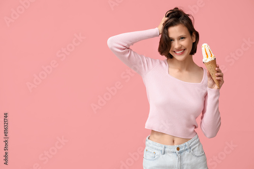 Beautiful young woman with sweet ice-cream in waffle cone on pink background