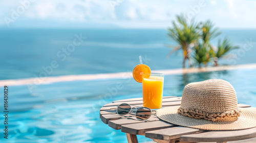 Beautiful summer background with pool and sunlounger, straw hat, sunglasses, orange juice on the table and sea view. Summer vacation concept