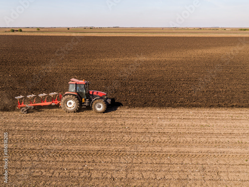 Aerial view of a tractor plowing rich soil in vast farmland during autumn season