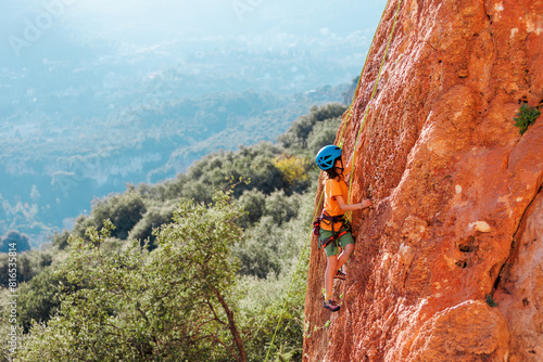 sport in summer camp. a child is rock climbing at a summer camp. rock climber boy. sport in nature on a sunny day. cute teenager climbs a rock with a belay. active holidays.