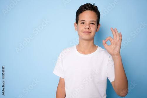 Portrait of a cheerful young boy showing okay gesture isolated on blue background