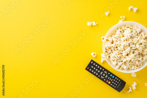 Enjoy home cinema with premieres via TV app. Top view of tasty popcorn and remote for online viewing. Yellow backdrop with space for text or ads